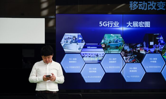 베이징의 한 통신사 밖 중국의 5G 산업을 보여주는 화면 앞에서 한 남성이 휴대전화를 사용하고 있다. 2019. 9. 25. | WANG ZHAO/AFP via Getty Images