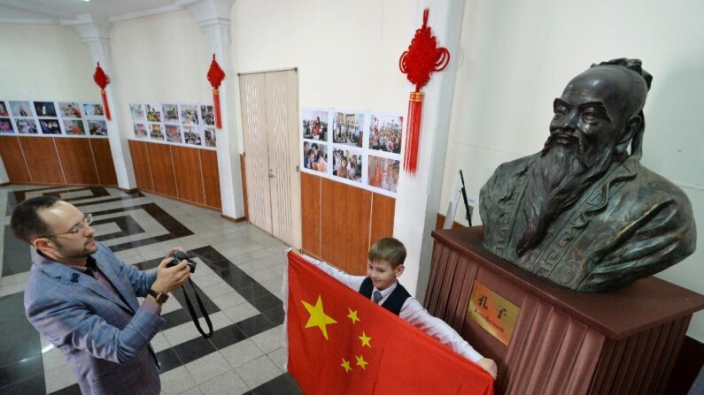 공자상 앞에서 중국 공산당 당 깃발인 오성홍기를 펼쳐든 서양인 초등학생을 학부모가 기념촬영하고 있다. | AFP=연합뉴스