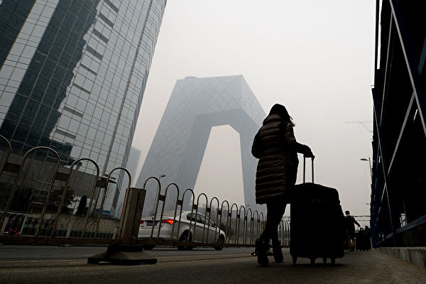 베이징 시내를 여행용 가방을 지니고 걸어가는 행인 뒤편으로 짙은 스모그와 함께 CCTV 청사 보인다. | STR/AFP via Getty Images 연합
