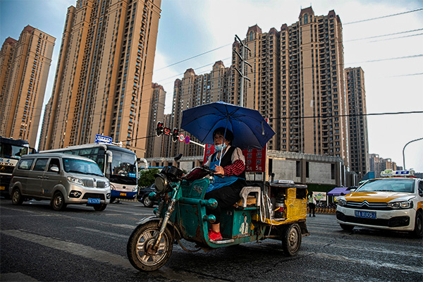 후베이성 ​​우한에서 한 중국 여성이 삼륜차를 운전하고 헝다 그룹이 개발한 한 아파트 단지 앞을 지나가고 있다. | Getty Images
