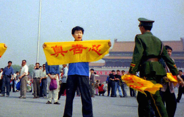 중국 베이징 톈안먼 광장에서 중국 경찰이 파룬궁 수련자에게 다가가고 있다. 수련자의 손에 들린 노란 현수막에는 파룬궁의 원칙인 진(眞)·선(善)·인(忍)이 적혀 있다. 경찰의 손에는 다른 수련자에게 빼앗은 것으로 보이는 같은 현수막이 들려 있다. 2001.5.13 | 밍후이왕